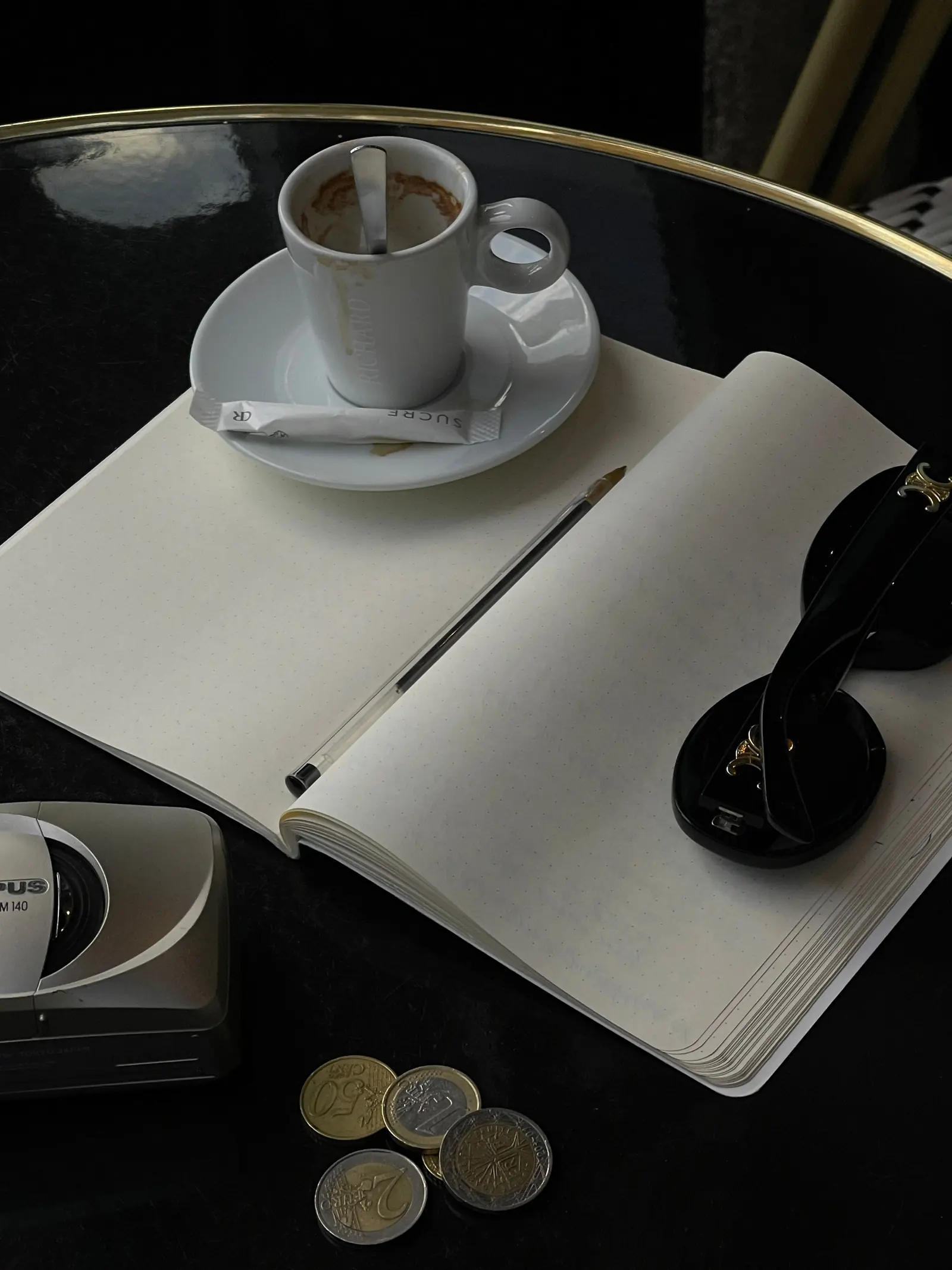 An espresso, an open journal, and sunglasses on a cafe table at dawn.