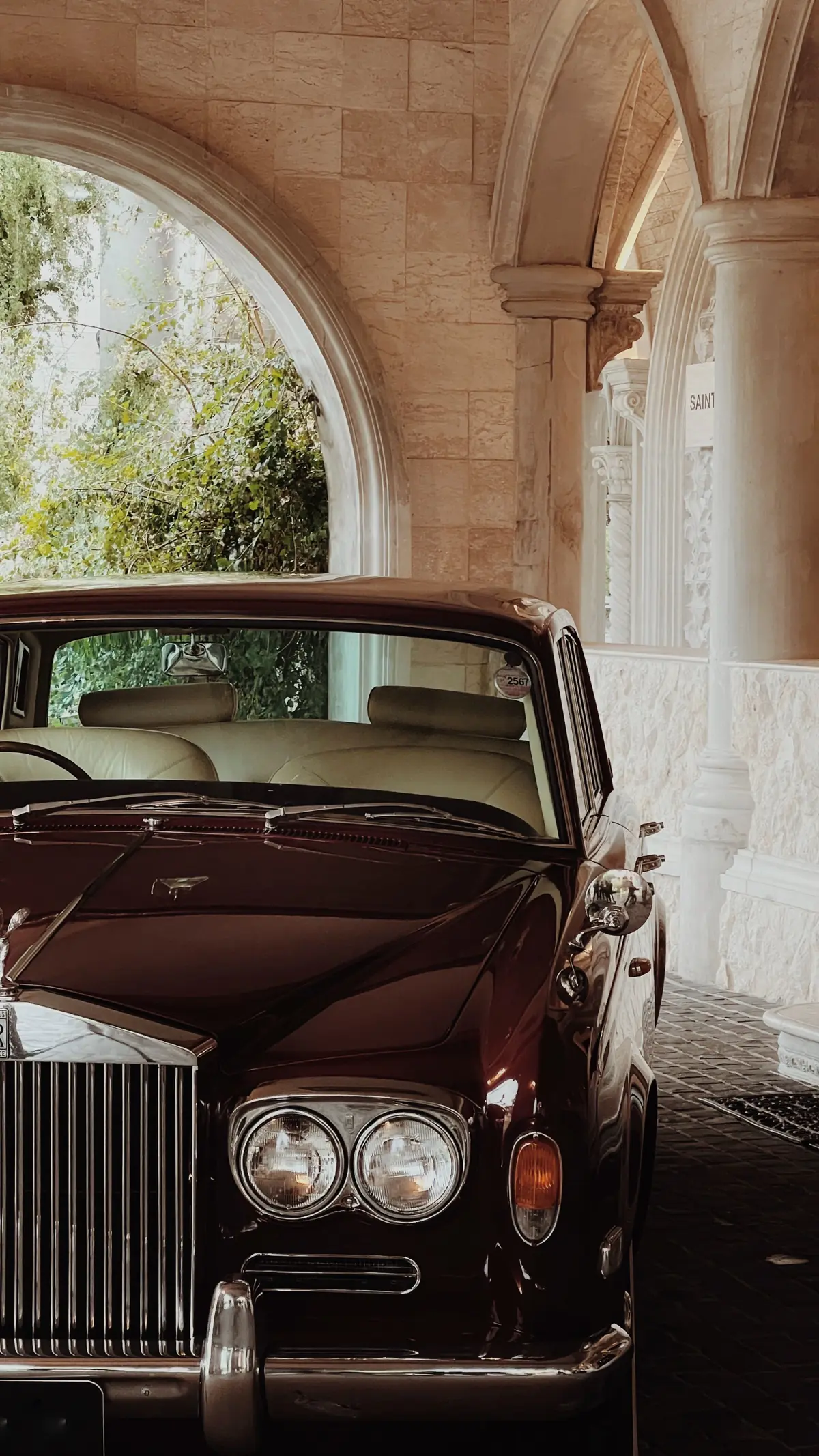 A vintage car parked under chandelier-lit stone arches inside a carriage house.